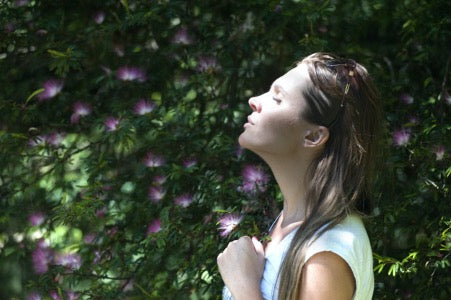 Women concentrating on breathing, she wears a white tshirt and is outside by a tree